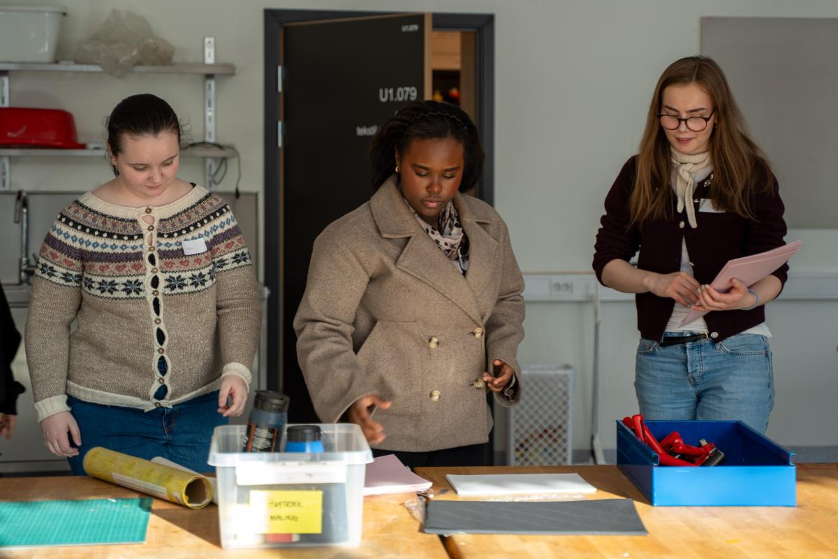 tre jenter holder ark og henter seg maling